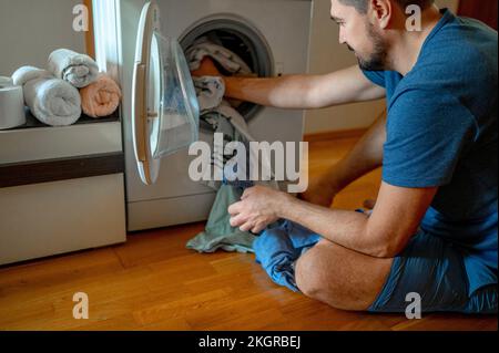 Man loading clothes in washing machine at home Stock Photo