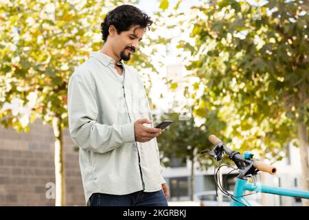 Smiling man using smart phone standing near bicycle Stock Photo