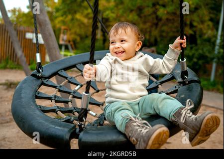 Happy cute baby boy swinging on nest swing at autumn park Stock Photo