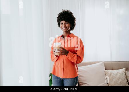 Happy freelancer standing with disposable coffee cup at home Stock Photo