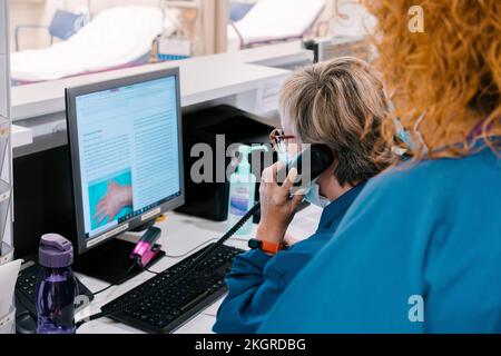 Nurse with colleague talking on telephone and using computer at hospital Stock Photo