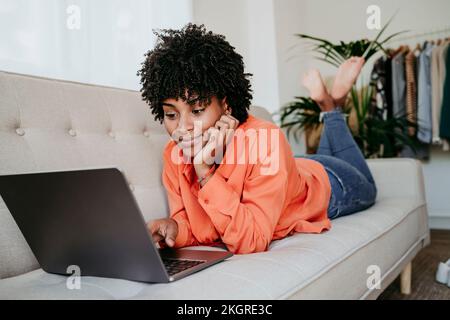 Freelancer lying on sofa and using laptop at home office Stock Photo