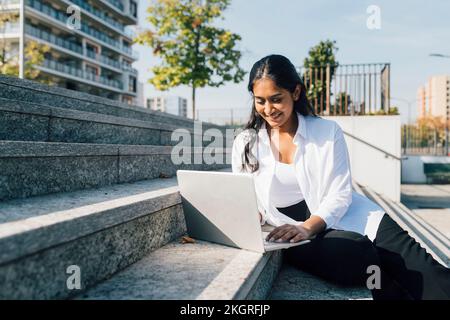 Smiling young woman using laptop on steps Stock Photo