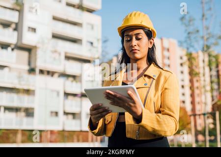 Woman wearing hardhat using tablet PC in front of buildings Stock Photo