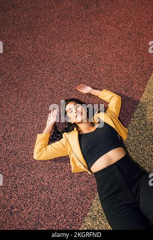 Smiling young woman in casuals lying at playground Stock Photo
