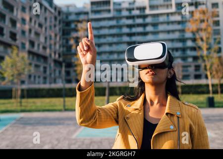 Young woman gesturing with virtual reality simulator in front of building Stock Photo