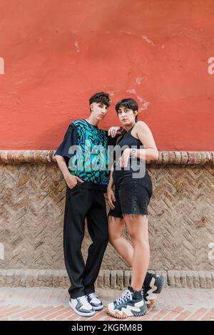 Young couple standing with hands in pockets leaning on wall Stock Photo