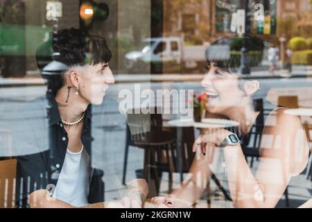 Happy young couple talking in cafe seen through glass Stock Photo