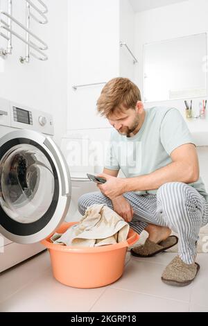 Man using smart phone by washing machine in bathroom at home Stock Photo