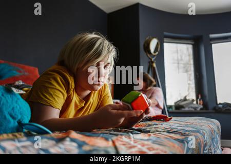 Boy playing with puzzle cube lying on bed at home Stock Photo