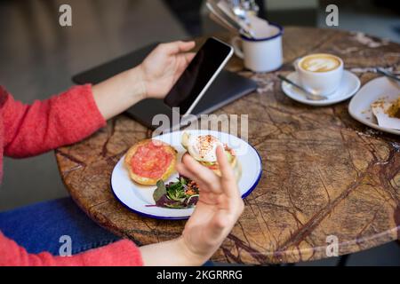 Freelancer using smart phone at table in cafe Stock Photo