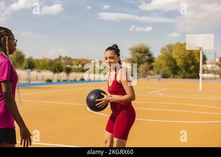 Young woman holding basketball in front of friend at sports court Stock Photo