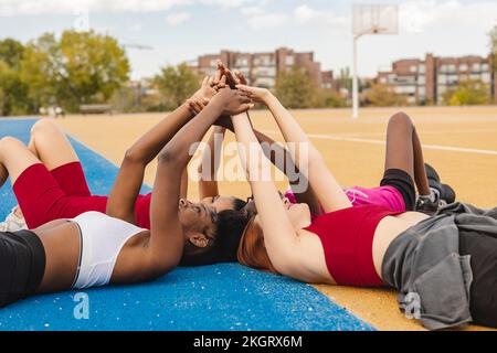 Young women lying down with hands raised in sports court Stock Photo