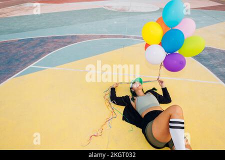 Happy woman holding colorful balloons lying on sports court Stock Photo