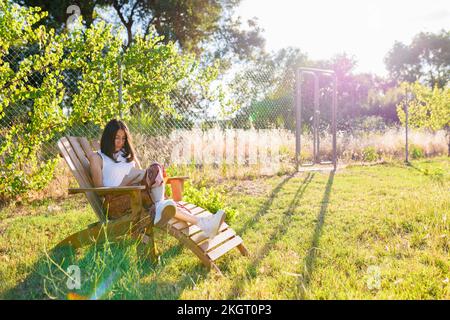 Mature woman reading book sitting in backyard on sunny day Stock Photo