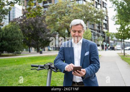 Smiling mature businessman using smart phone to unlock electric push scooter Stock Photo