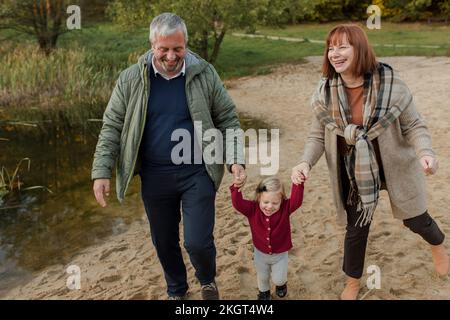 Grandparents walking on sand with granddaughter Stock Photo