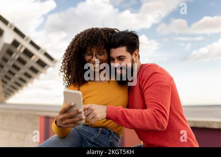 Happy young couple using smart phone under cloudy sky Stock Photo