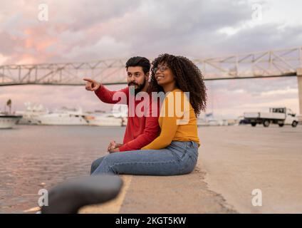 Young man gesturing with woman sitting on promenade at sunset Stock Photo
