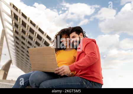Happy young couple using laptop under cloudy sky Stock Photo