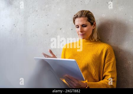 Businesswoman using tablet computer in front of wall Stock Photo