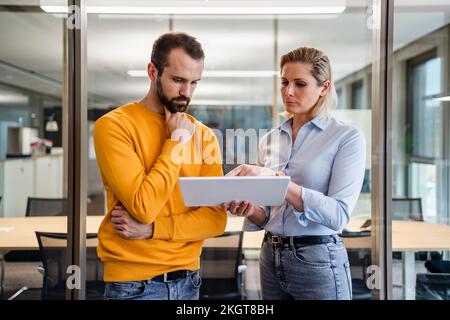 Businessman with hand on chin looking at tablet PC held by colleague in office Stock Photo