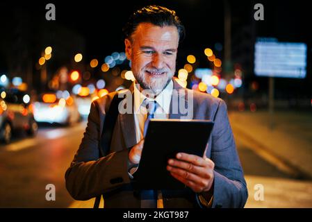 Happy mature businessman using tablet PC at night Stock Photo