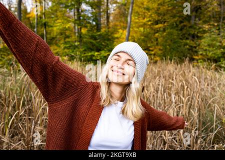Smiling mature woman with eyes closed and arms outstretched in meadow Stock Photo