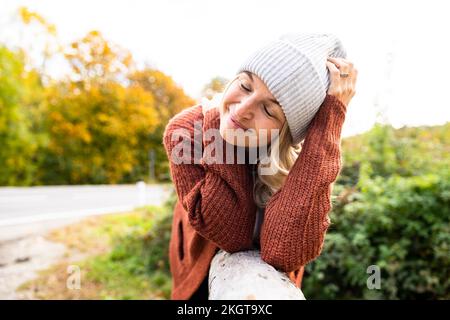 Smiling mature woman with eyes closed leaning on wood Stock Photo