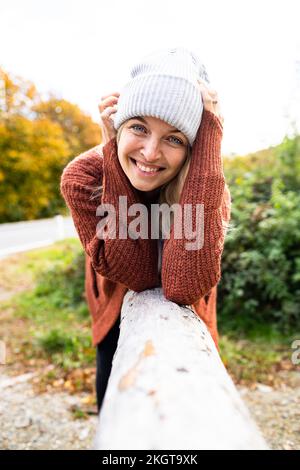 Smiling mature woman leaning on wood in autumn Stock Photo