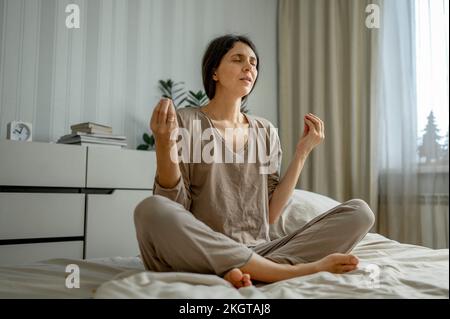 Woman meditating sitting on bed at home Stock Photo