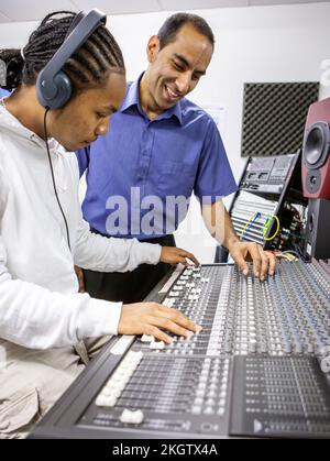 Music Students: Audio Mixer. A young sound engineer learning to use a music studio mixing desk with his teacher. From a series of related images. Stock Photo