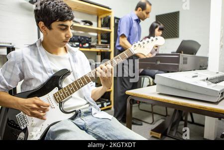 Music Students: Playing Together. A young guitarist practicing chords while teacher helps his keyboard player. From a series of related images. Stock Photo