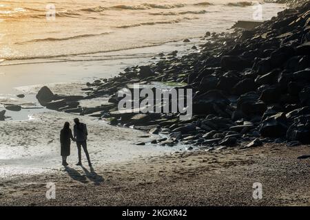 A young couple in sillhouette holding hands on a beach in Lyme Regis, Dorset, England Stock Photo