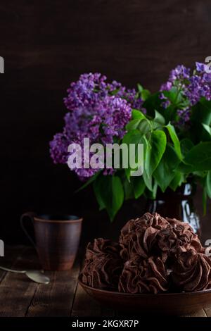 coffee zepfyr on a wooden background in a plate, in the background - a cup of coffee, lilac branches. Stock Photo