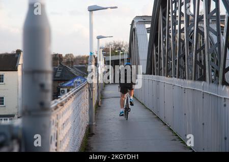 23rd November 2022. London, UK. Barnes Railway Bridge Closed for Urgent Repairs.A solitary cyclist on the footbridge next to Barnes Railway Bridge, a Victorian Grade II structure, is closed for urgent repairs to 4 of the 86 steel pins which hold in place the structural girders supporting the railway tracks. There will be no trains between Chiswick and Waterloo until perhaps the New Year with a diverted service to Kew Bridge for commuters. Credit Peter Hogan/ALAMY Stock Photo
