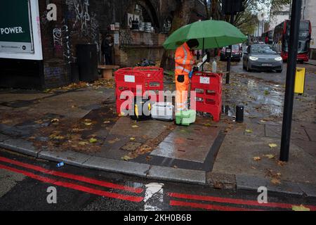 A telecoms engineer for an unknown company works at the kerbside in a Waterloo street during a rain shower in south London, on 23rd November 2022, in London, England. Stock Photo