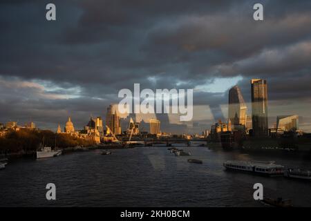 Seen from the top deck of a London bus that is driving over the river Thames on Waterloo Bridge, are the tall towers of the City of London - including the dome of St Paul's Cathedral - and on the right, the Southbank, all seen in late afternoon autumn sunlight, on 22nd November 2022, in London, England. Stock Photo