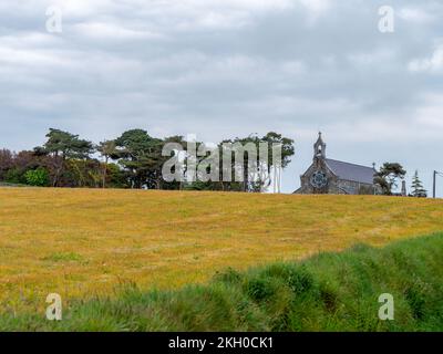 A small stone Christian church in the distance of a beautiful meadow. Cloudy sky, European landscape. Green and yellow grass field with trees under wh Stock Photo