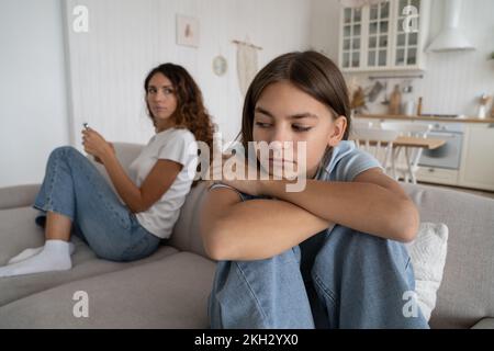 Offended teen girl feeling sad after argument with parent, sitting separately with mother on sofa Stock Photo