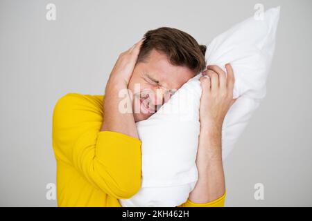 Portrait of Young Caucasian man in bed angry about noise  Stock Photo