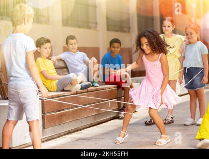 Energetic kids playing and skipping on elastic jumping rope in yard Stock Photo