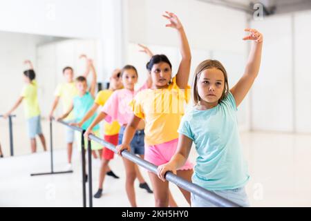 Children standing along ballet bar in dance studio during dance class Stock Photo