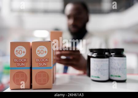 African american pharmacist taking sunscreen from drugstore shelf, closeup selective focus. Pharmacy concept, summer skin care selling, medical supplement in apothecary, close view Stock Photo