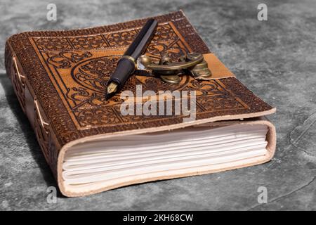 Leather journal, embossed with Celtic tree of life design, with recycled paper and fountain pen. On a dark stone background Stock Photo