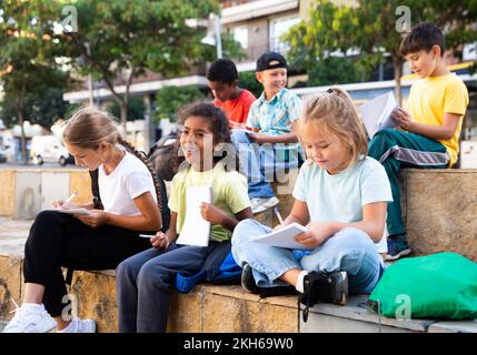 Tweenagers studying outside school, writing in workbooks Stock Photo