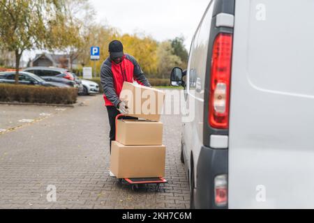 Modern blue-collar-workers. Full-length outdoor shot of a handsome ethnic male courier reading delivery labels placed on cardboard boxes. Online shopping process. High quality photo Stock Photo