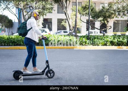 Man with headphones riding an electric scooter on a city street Stock Photo