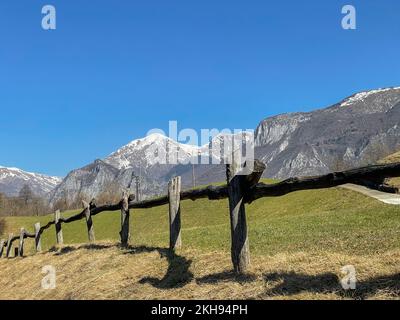 Wooden fence, green grass and snowy mountains under the blue sky. Beautiful nature scenery on bright sunny day. European mountain landscape. Peaceful Stock Photo