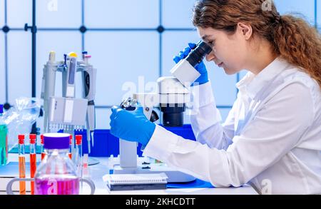 young adult female student working with a microscope examining biological samples using a microscope in a genetic laboratory Stock Photo